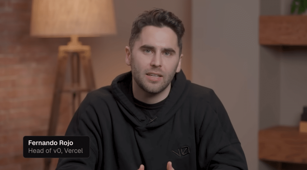 A man with short dark hair and a trimmed beard, wearing a black hoodie, sits indoors and looks at the camera during a remote demo. On the screen, text reads 